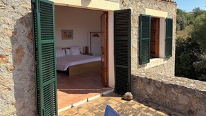 A stone building with a bedroom featuring a bed, a nightstand, and a lamp. The room has green shutters and a tiled floor. - Fetget, quiet rural property with swimming pool. (IB)