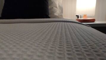 A bed with a textured white cover, a black pillow, a white pillow, and a bedside table with a lamp.