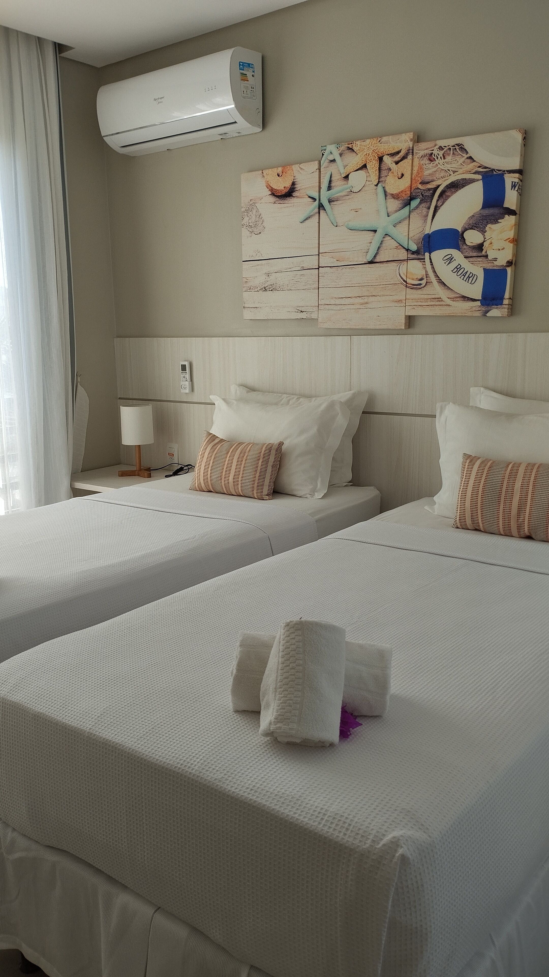 Ein Hotelzimmer mit zwei Betten, einer Wandklimaanlage, einem Gemälde und einer Lampe.