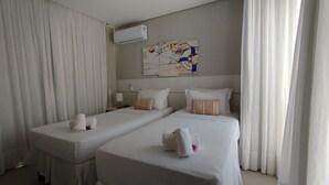 A hotel room with two beds, white bedding, striped pillows, and a beach-themed artwork on the wall. - Villa Preziosa Front Beach (Fleicheiras)