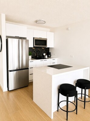 Una cocina moderna con un refrigerador de acero inoxidable, un microondas y una cafetera sobre la encimera.