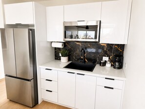 Een moderne keuken met een roestvrijstalen koelkast, witte kasten, een zwart en goudkleurige spatwand en een inbouwmagnetron.