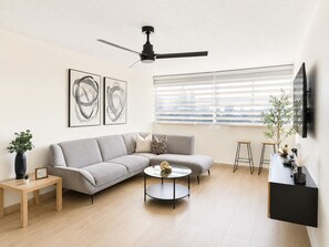 Una sala de estar moderna con un sofá gris, una mesa redonda de centro y un ventilador de techo.