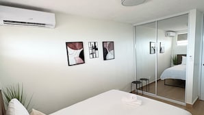 A modern hotel room with a large bed, a wall-mounted air conditioner, and a mirror reflecting the room. - Cityscape Escape/Art District Vibes/Bay & City Views (San Juan)