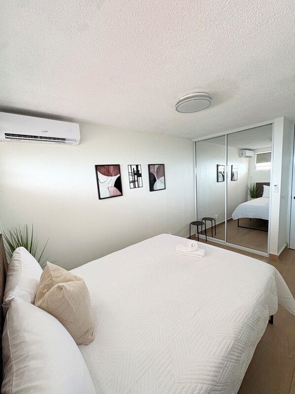 Ein modernes Hotelzimmer mit einem großen Bett, einer Wandklimaanlage und einem Spiegel, der den Raum wiederspiegelt.