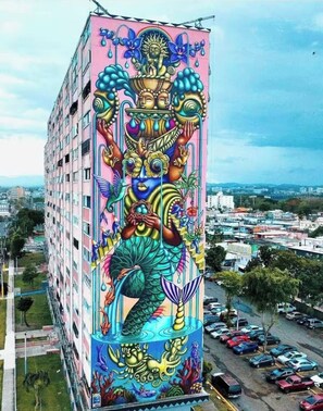 A tall building with a colorful mural featuring a mermaid, sun, and various abstract elements.