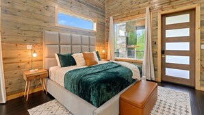 Une chambre à coucher aux murs lambrissés, avec un lit, une table de chevet et une vue sur l’extérieur.