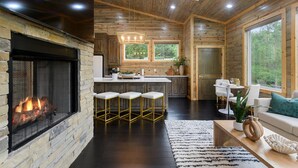Un intérieur moderne de chalet en bois avec une cheminée en pierre, une cuisine dotée de tabourets de bar, un coin repas et de grandes fenêtres offrant une vue sur l’extérieur.