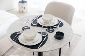 A round dining table with a speckled marble top, black placemats, and white plates and bowls. - JVC Studio for 2 People With City Views (Dubai)