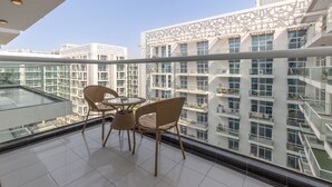 Ein Balkon mit Korbmöbeln und einem Glastisch, mit Blick auf ein modernes Gebäude mit gemustertem Fassade und mehreren Balkonen.