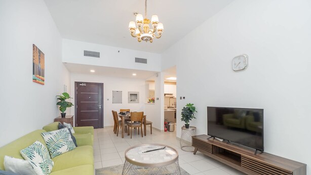 Ein modernes Wohnzimmer mit einem grünen Sofa, einem Couchtisch, einem Fernseher auf einem Holzständer und einem Essbereich mit Stühlen und einem Tisch.