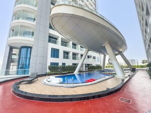 Un edificio moderno con zona de piscina, que incluye una estructura de sombrilla y sillas de descanso.