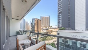 Un balcón con dos sillas y una mesa pequeña, con vistas a un paisaje urbano con edificios altos.
