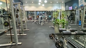 Een fitnessruimte met diverse trainingsapparaten, waaronder krachttoestellen en losse gewichten, en spiegels aan de muur.