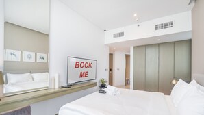Una habitación de hotel moderna con una cama grande, una mesita de noche, un espejo y un televisor montado en la pared que muestra “BOOK ME”.