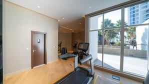 Un gimnasio con cintas de correr y equipo de ejercicio, ventanas amplias y una puerta.