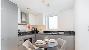 Una cocina moderna con armarios grises, una isla central y un área de comedor con dos sillas grises y una mesa pequeña.