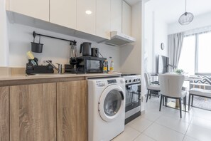Una cocina moderna con lavadora y secadora integradas, cafetera y zona de comedor con sofá y sillas.