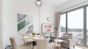Un salon moderne avec un coin repas, une grande fenêtre donnant sur la ville, une horloge et un panneau indiquant « RÉSERVEZ-MOI ».