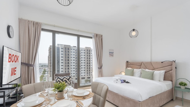 Une chambre d’hôtel moderne avec un grand lit, un coin repas avec une table dressée pour quatre personnes, et une vue sur les gratte-ciel.