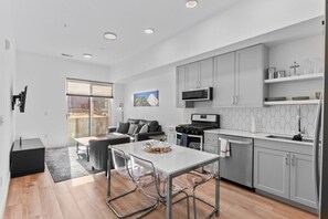 A modern kitchen with grey cabinets, a black stove, and a microwave. There is a dining area with a white table and chairs. - Modern 2B Condo with Sofa Sleeper (Denver)