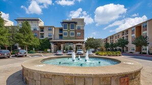 A hotel with a central courtyard featuring a fountain, surrounded by multi-story buildings with a modern architectural style. - Charming & Cozy 1BR/1BA/2BEDS. Pool/Gym/Shops (Frisco)