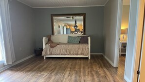 Ein Zimmer mit Holzboden, einem weißen Sofa mit brauner Decke und einem großen Spiegel, der eine Küche widerspiegelt.