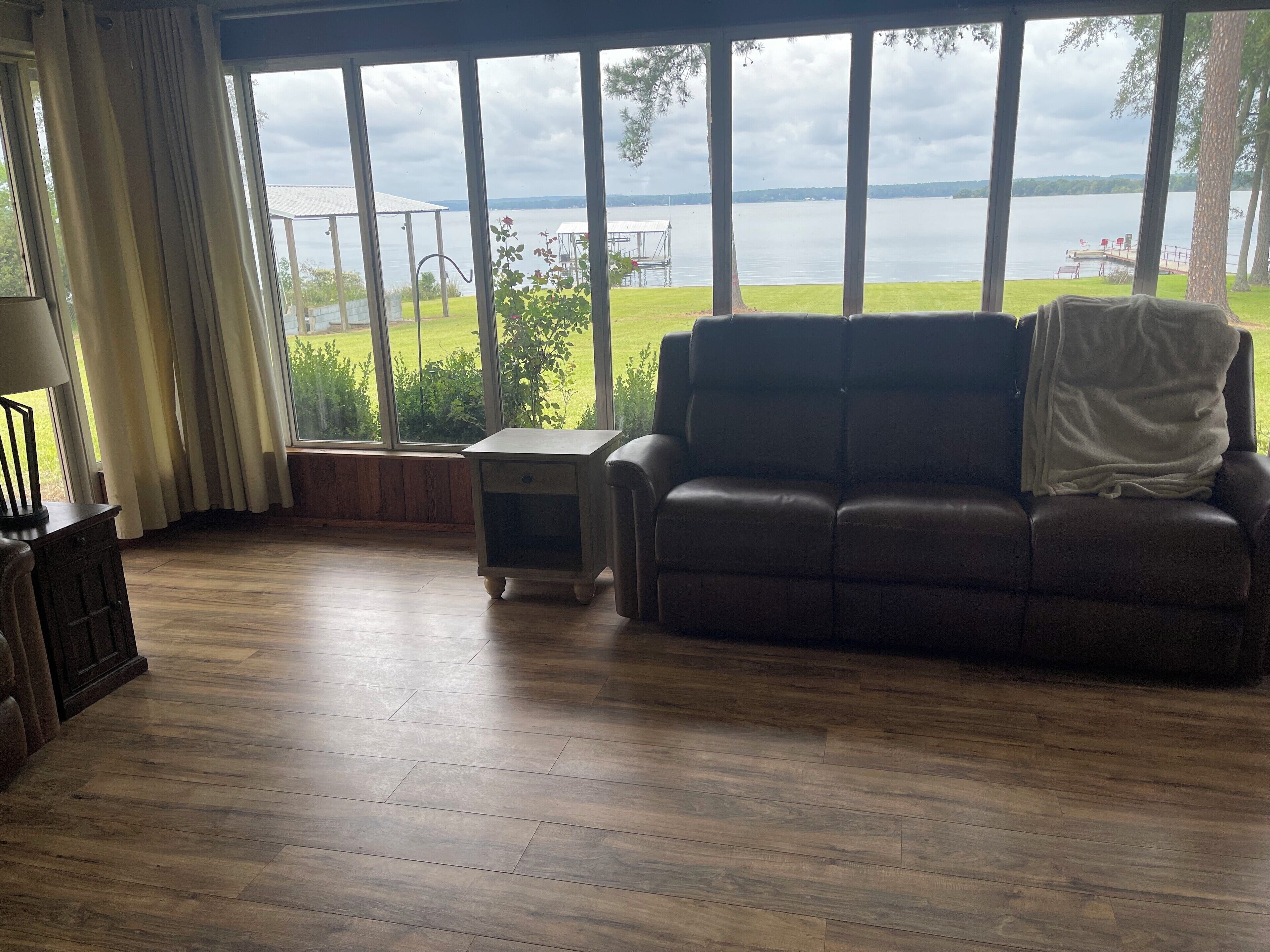 A living room with a large window, a brown leather sofa, a small table, and a lamp.