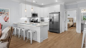 A modern kitchen with white cabinetry, stainless steel appliances, and a central island with bar stools. - Spacious 4 Bedroom 3.5 Bathroom walking distance to the beach. Close proximity! (Myrtle Beach)
