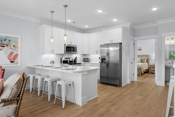 A modern kitchen with white cabinetry, stainless steel appliances, and a central island with bar stools.