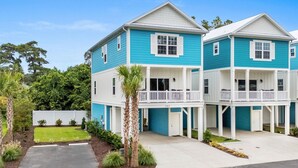 A two-story residential building with a blue exterior and white trim, featuring a covered front porch and a small balcony on each floor. - Spacious 4 Bedroom 3.5 Bathroom walking distance to the beach. Close proximity! (Myrtle Beach)