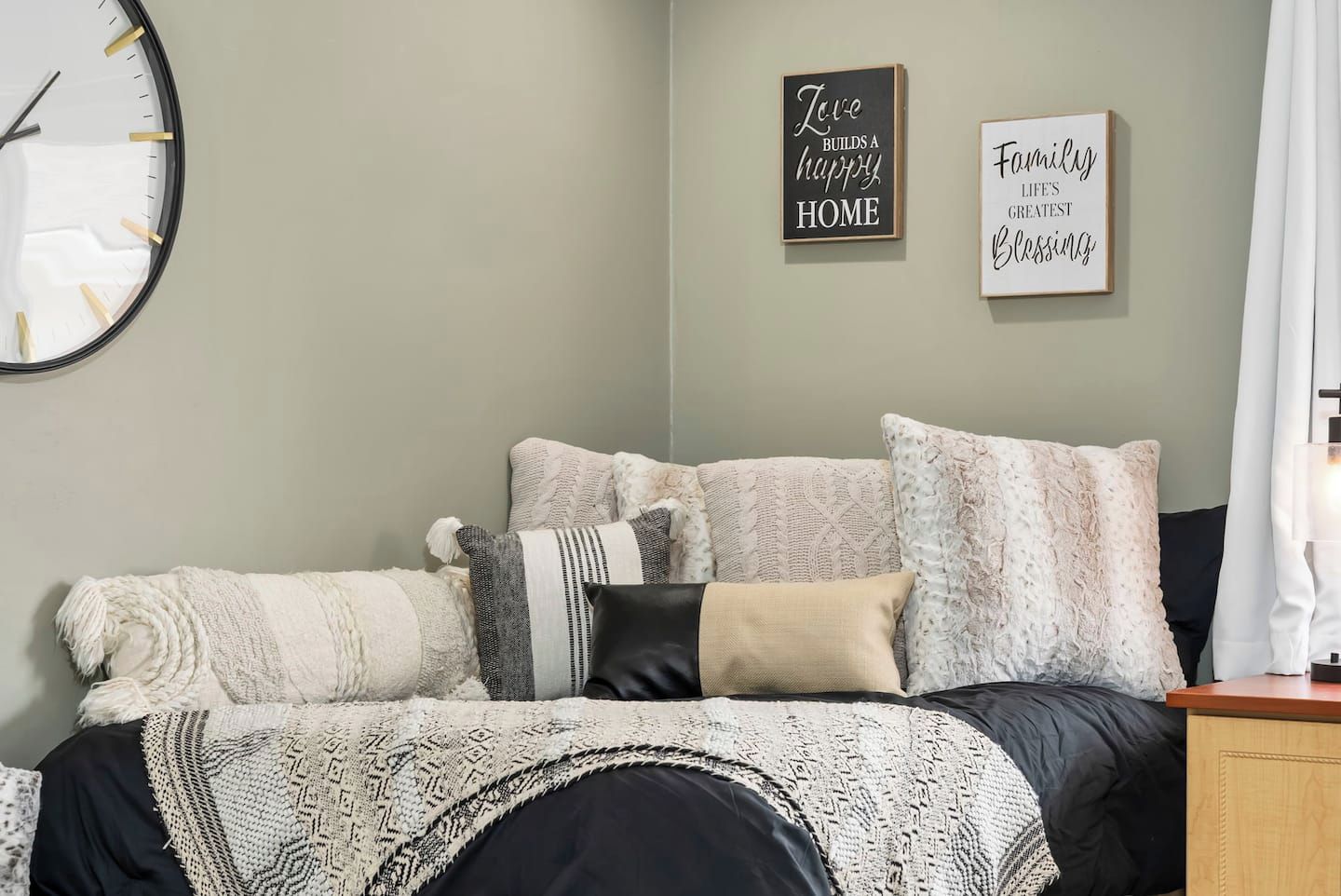 A bedroom with a bed, pillows, a wall clock, and two motivational wall art pieces.