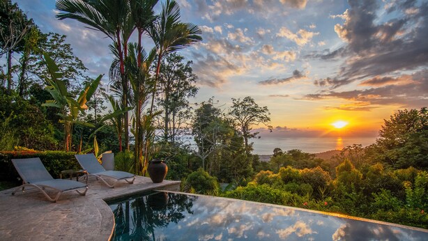 Ein Pool mit Liegestühlen und Blick auf den Sonnenuntergang über dem Meer.