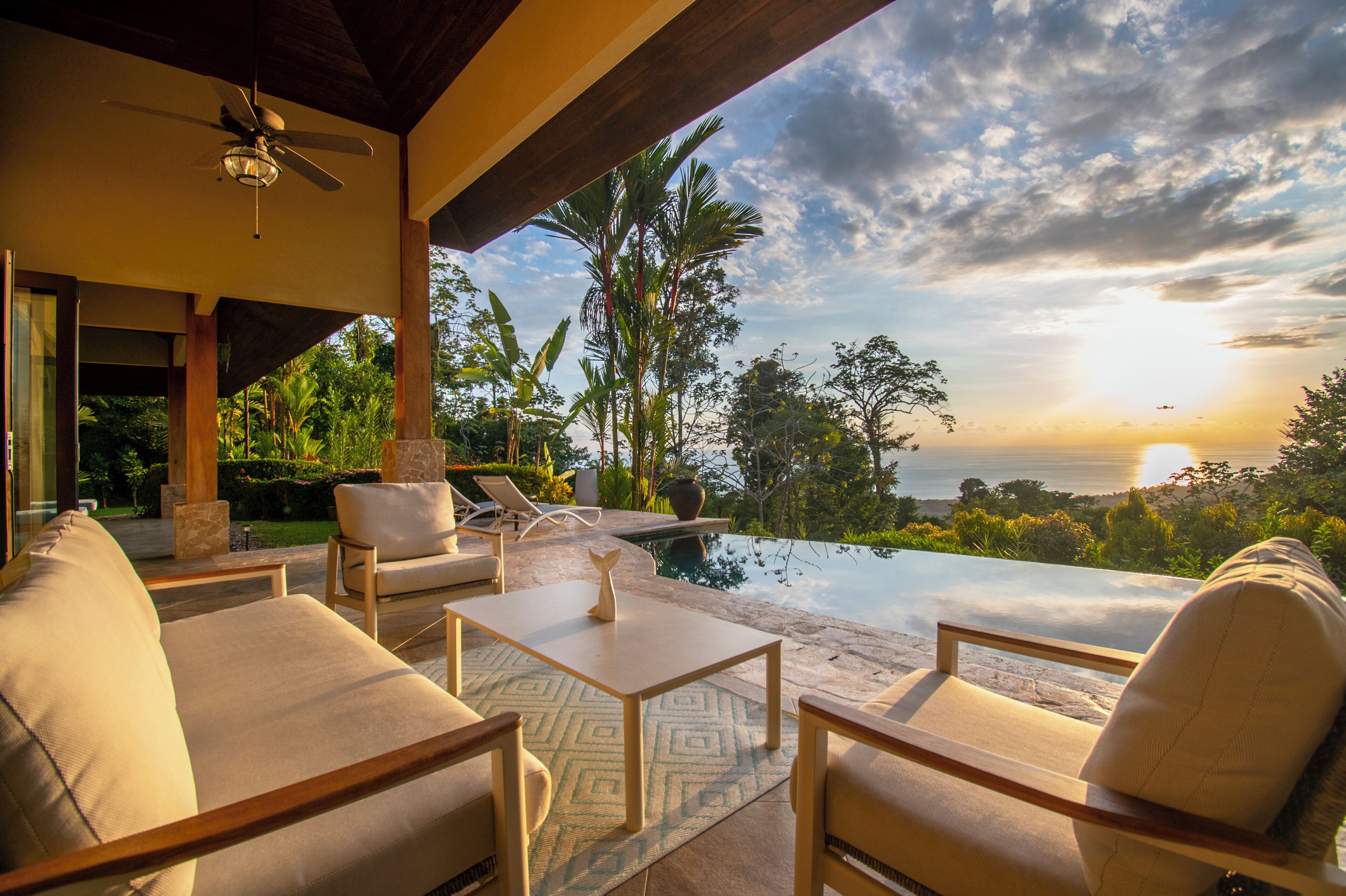 A poolside area with lounge chairs, a table, and a view of the ocean at sunset.