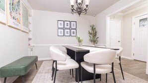 Un coin repas comprenant une table ronde, quatre chaises, un banc et des œuvres d’art encadrées accrochées au mur.