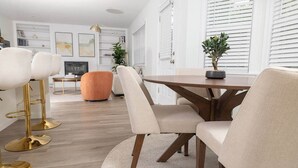 Un espace repas moderne avec une table en bois, des chaises recouvertes d’un tissu beige et un lampadaire doré.