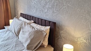 A neatly made bed with a headboard, a bedside lamp, and a wall with a leaf pattern. - Free Parking, Greater London & Kent Gateway (New Addington)