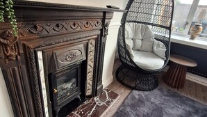 A fireplace with intricate carvings, a hanging chair with a cushioned seat, and a view of the outside through a window.