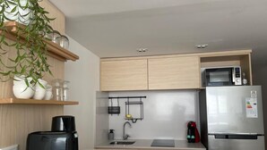 Una cocina moderna con armarios de madera clara, un refrigerador de acero inoxidable, un microondas, un tostador y una planta colgante.