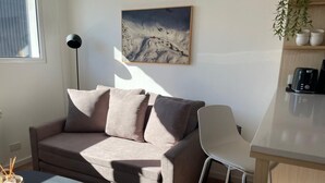 Una sala de estar moderna con un sofá, una mesita, una cafetera y un cuadro en la pared.
