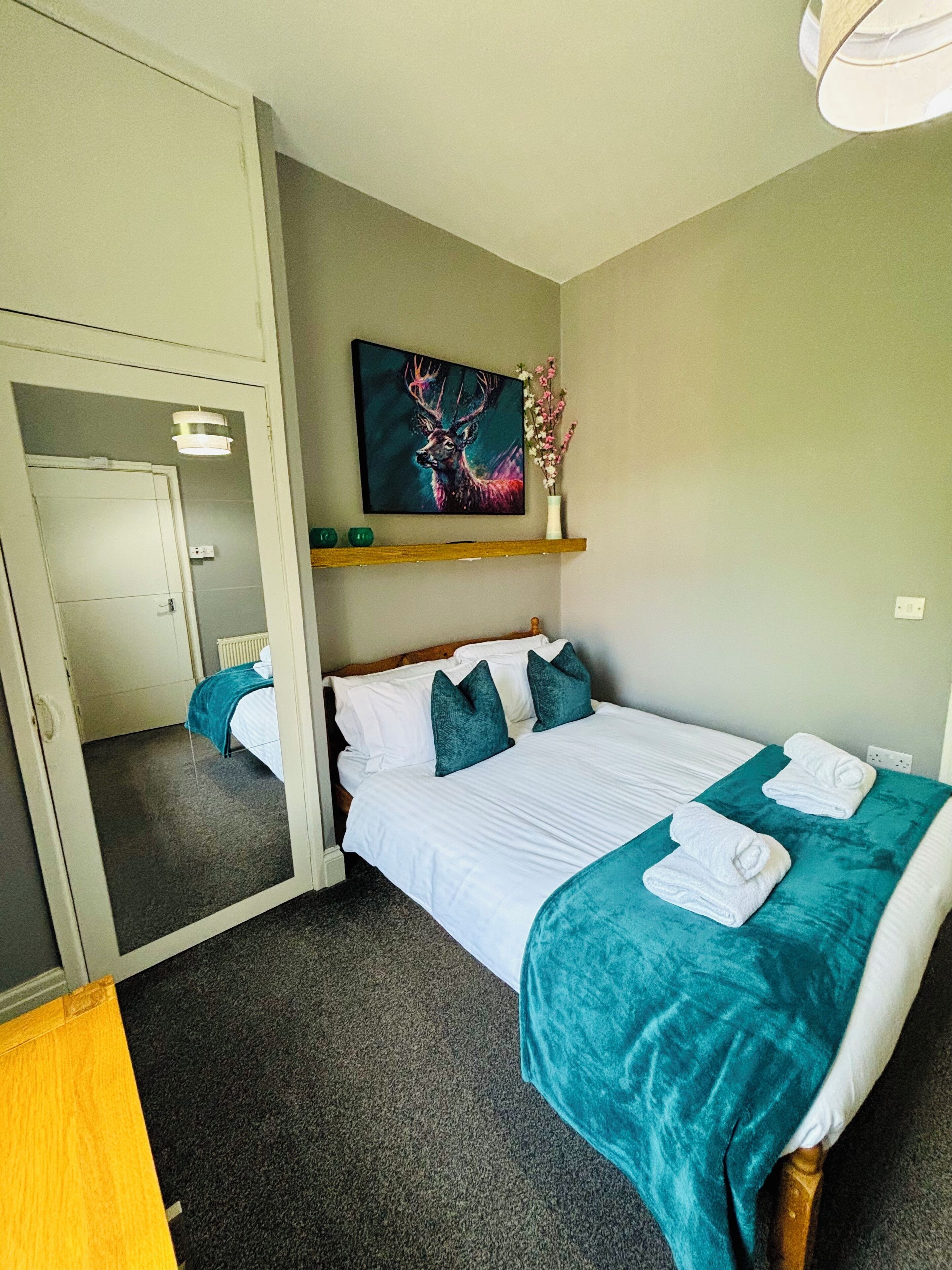 Una habitación de hotel con una cama, un cuadro, un jarrón con flores y un espejo.