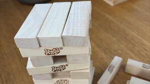 A stack of wooden blocks with the brand name "Jenga" on them, placed on a wooden table.