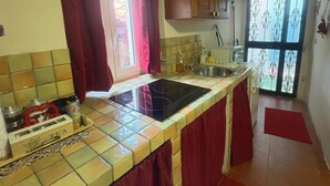 Uma cozinha com painel de azulejos, armários de madeira, fogão preto e janela com cortinas vermelhas.