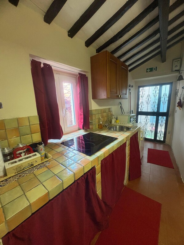 A kitchen with a tiled backsplash, wooden cabinets, a black stove, and a window with red curtains.