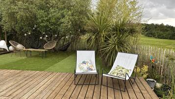 A wooden deck with two lounge chairs, a hammock, and a small table.