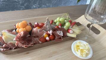 Una tabla de madera con varios quesos, embutidos, frutas y una copa de vino.