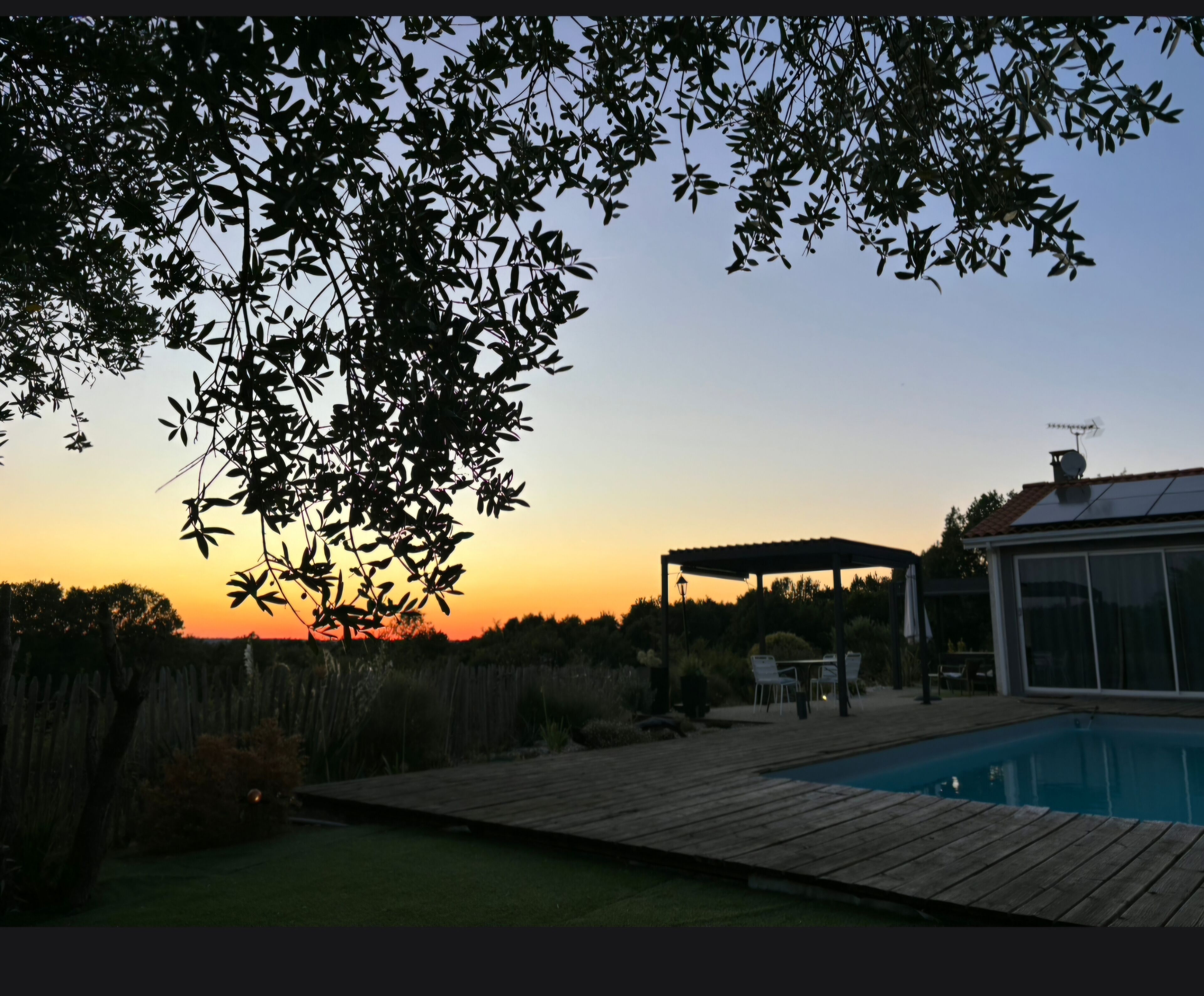 Un patio trasero con terraza de madera, piscina y un área de patio cubierto.