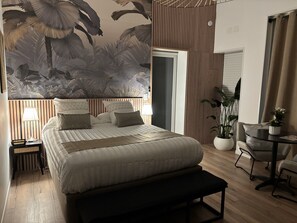 A bedroom with a large bed, bedside lamps, a bench, a small table with a plant, and a wall mural.