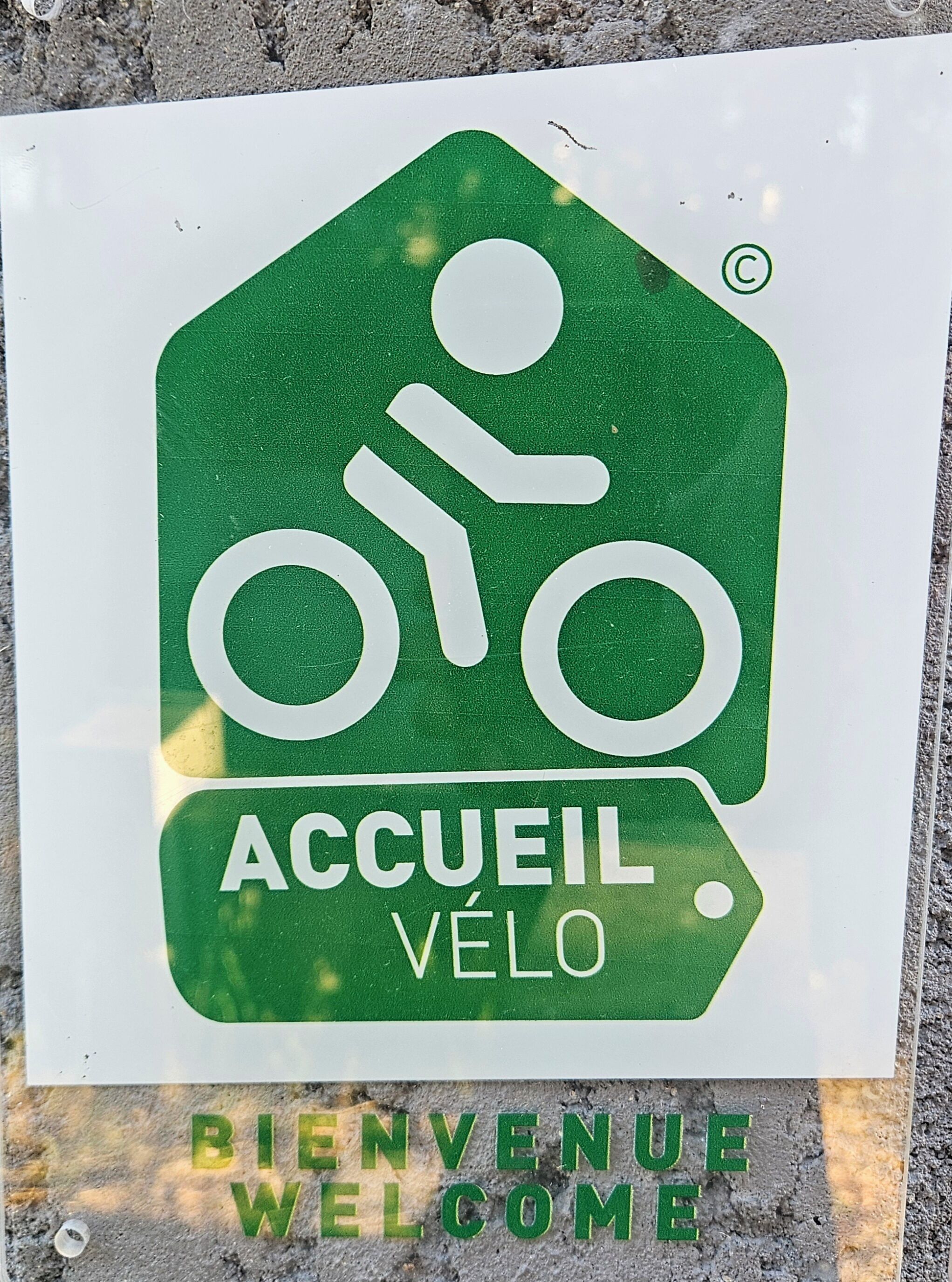 A green welcome sign with a bicycle symbol and the words 'ACCUEL VÉLO' and 'BIENVENUE WELCOME' on a white background.