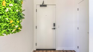 En hvid dør med et moderne håndtag og en sikkerhedsanordning, en grøn væg med planter og et trægulv.